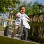 Jong kind fietst vrolijk op houten loopfiets met schaap