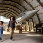 Kinderen rennen door een hangar met straaljagers