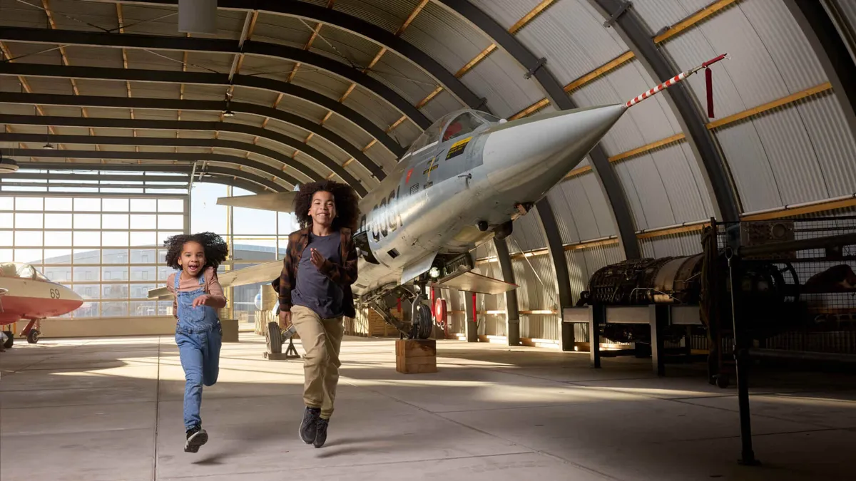 Kinderen rennen door een hangar met straaljagers