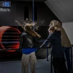 Drie bezoekers trotseren de windstroom van 139 km/u in de stormsimulator van Deltapark Neeltje Jans.