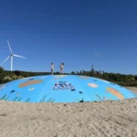 Twee kinderen springen hand in hand op een luchtkussen bij Deltapark Neeltje Jans met een windmolen op de achtergrond.