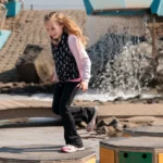 Lachend meisje rent over houten stapstenen in een interactieve waterspeeltuin bij Deltapark Neeltje Jans.