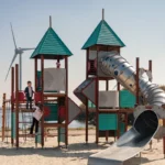Kinderen spelen op een kleurrijk klim- en glijtoestel op het strand van Deltapark Neeltje Jans met uitzicht op het water.