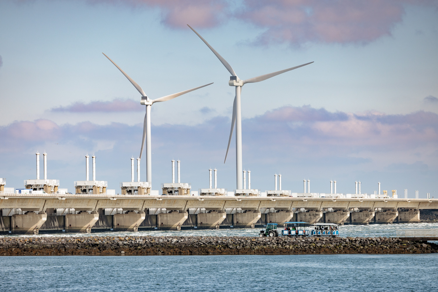 De Oosterscheldekering met twee grote windmolens en een toeristentreintje op de voorgrond.