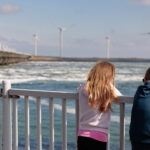 Een gezin kijkt samen uit over het landschap richting de windmolens en de stormvloedkering.