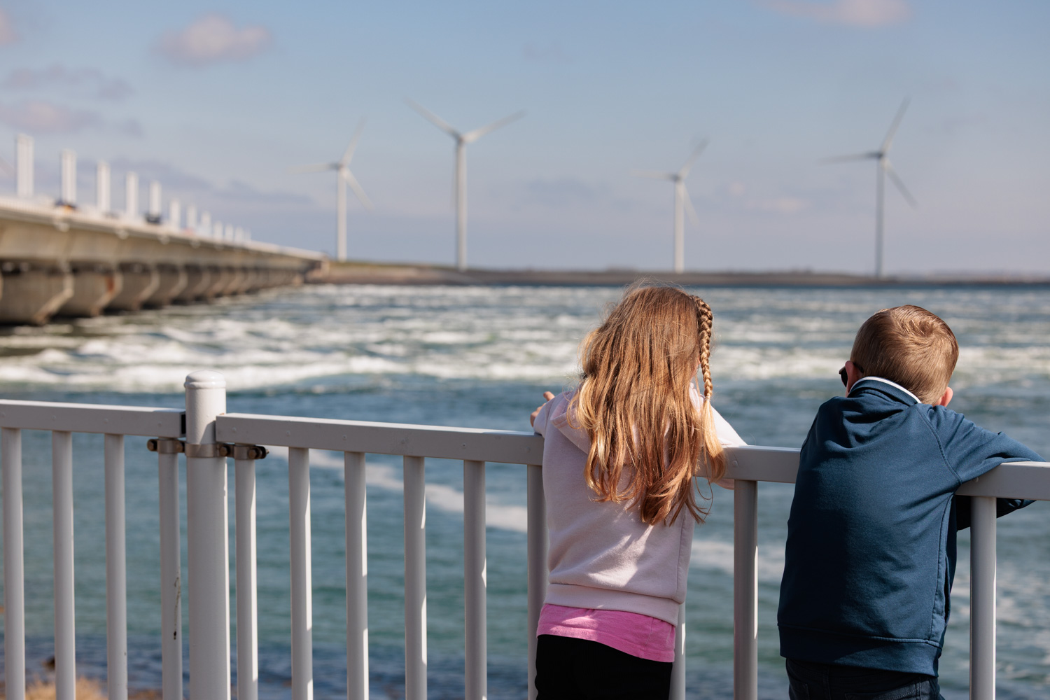 Een gezin kijkt samen uit over het landschap richting de windmolens en de stormvloedkering.