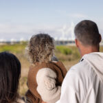 Gezin wandelt op een zonnige herfstdag bij Deltapark Neeltje Jans met uitzicht op de Oosterschelde, blauwe lucht en zachte branding op de achtergrond.