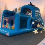 Een groot blauw onderwater-thema springkussen staat in een fictief winterlandschap met besneeuwde bomen en warm zonlicht.